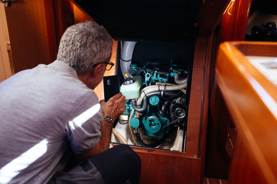 Senior mechanic checking engine with cellphone flashlight