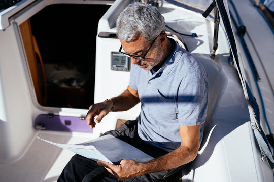 Stylish mature man in glasses reading on sailboat