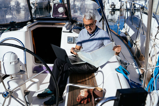 Focused senior helmsman examining document on sailboat