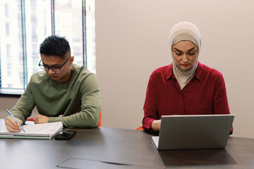Female muslim employee typing on laptop near male colleague