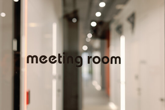 Text on glass door of meeting room with blurred hall on background