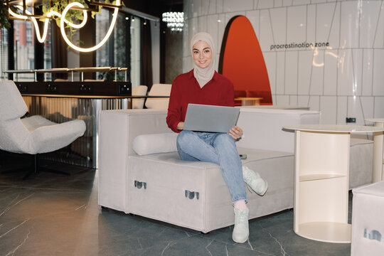 Young muslim female IT company developer working on laptop on armchair