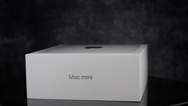 Unopened white box of an Apple Mac mini computer sitting on a dark glass surface with a dark background - FRANKFURT, GERMANY - MAY 02, 2025