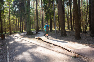 A 12 year old boy in a cap and shorts rides a scooter on a pump track in Borovsky Park in Moscow in the spring.	