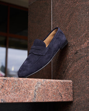 Elegant navy suede loafers showcased on a stone pedestal
