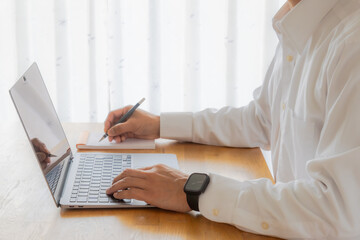 メモを取りながらノートパソコンで作業をする男性の手元