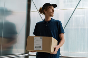 Portrait of courier with box in elevator