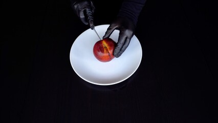 Slicing nectarine in black gloves.
A man in black clothes and gloves carefully cuts a nectarine with a knife on a white plate. Clean, minimalistic background.