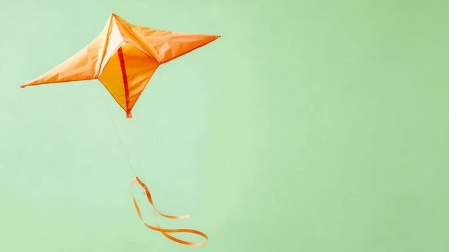 Orange kite flying in pale green background.