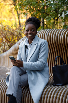 Stategy consultant sitting on bench in park with smartphone in hands