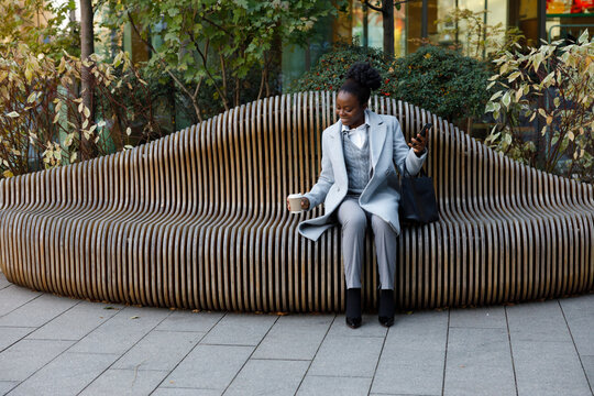 Happy investor drinking coffee on bench outdoors after making deal