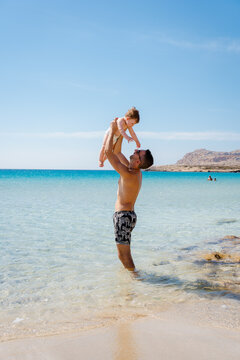 A man holding his son as they enjoy a day at the beach in summer