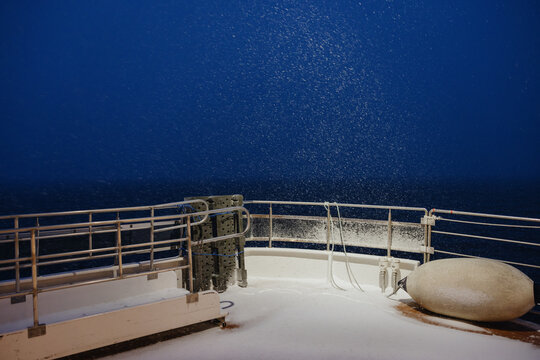 Snowfall on boat deck at night over dark sea
