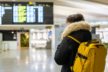 Woman with yellow backpack looking at timetable in airport terminal