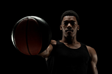 Basketball player holding a ball against black background. Serious concentrated african american...