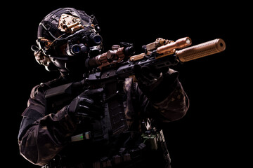 Tactical operative wearing night vision gear and aiming a modern camouflaged weapon