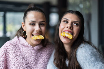 Two young women smiling while biting lemon slices in a playful and fun moment