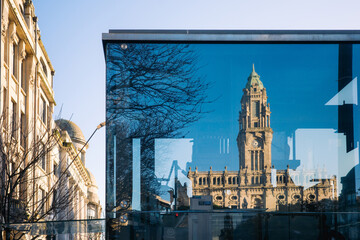 Glass reflection of historic clock tower in urban setting
