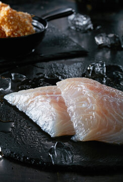 Fresh fish pieces with ice cubes on black cutting board