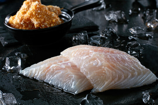 Fresh fish pieces with ice cubes on black cutting board