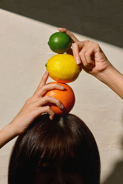 Hands Balancing Lime, Lemon, and Orange Over a Person's Head