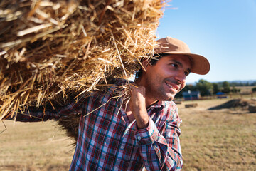 Latin American farmer carrying hay bale in field