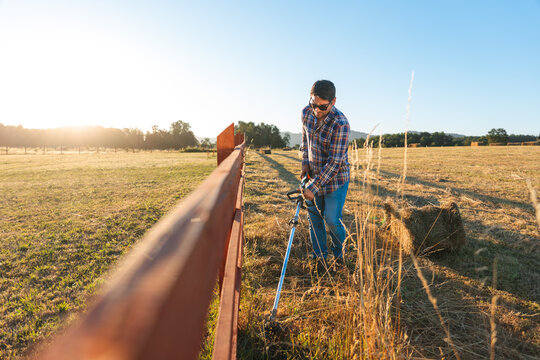 Latin farmer cutting grass along fence in field