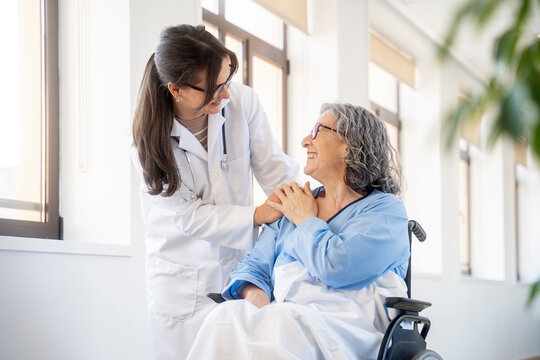 Young doctor comforting senior patient in wheelchair in hospital