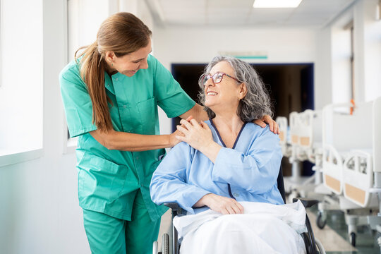 Doctor comforting elderly patient in wheelchair in hospital corridor