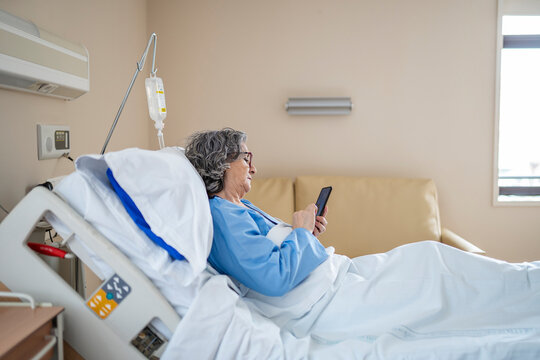 Senior patient using smartphone while resting in hospital bed