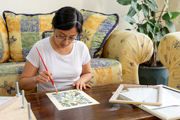 Woman using a paintbrush to clean a handmade artwork of dried flora
