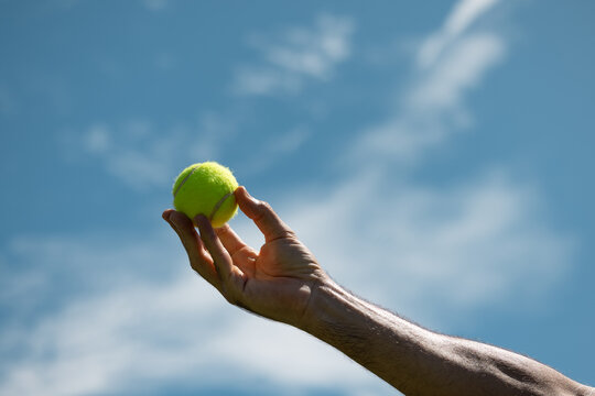 Hand holding tennis ball against blue sky background
