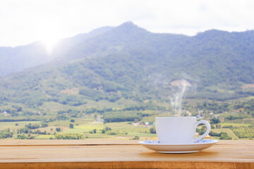 Cup of hot coffee on a wooden table, natural scenery backdrop, mountain views, Warm morning sunlight