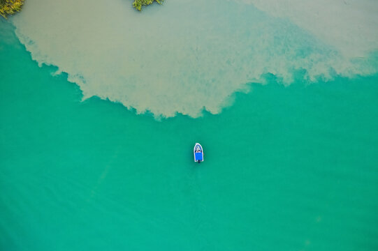 Small boat on green lake with cloudy water along the shoreline