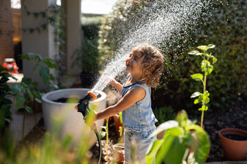 Toddler laugh as she sprays herself with the water hose.