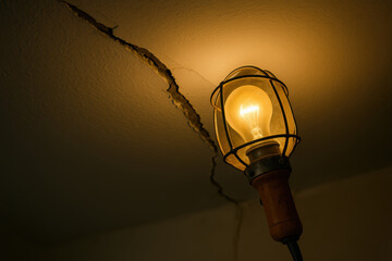 Illuminated light bulb on antique fixture revealing ceiling crack in dim room