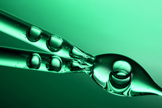 Close up of a pipette dispensing liquid on gradient green background.