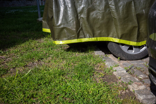 Covered vehicle with green tarp parked on grass and cobblestone