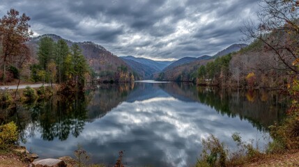 Fototapeta premium Serene autumnal lake reflecting a cloudy mountain sky.