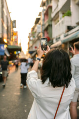 Tourist taking pictures of bangkok street at sunset with smartphone