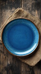 Blue ceramic dinner plate on rustic burlap fabric over rough wooden surface
