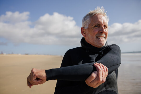 Senior Man Stretching on Sandy Beach During a Sunny Day