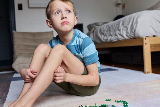 Little boy with eczema sits on a rug upset