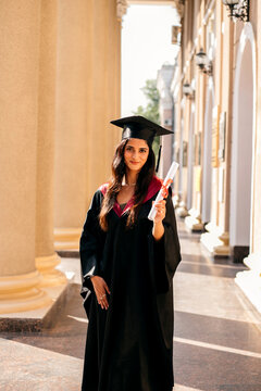 Indian woman wearing graduated uniform holding diploma at university.