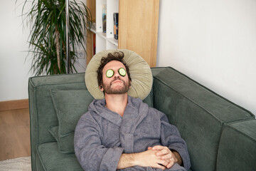 man on sofa with sliced ​​cucumbers on his eyes
