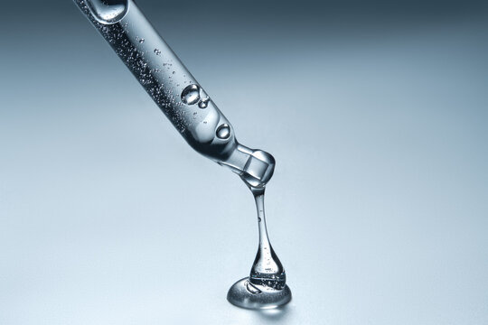Clear glass pipette with a drop of cosmetic product falling down. 