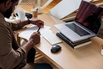 Man reading business documents by laptop on desk at home office