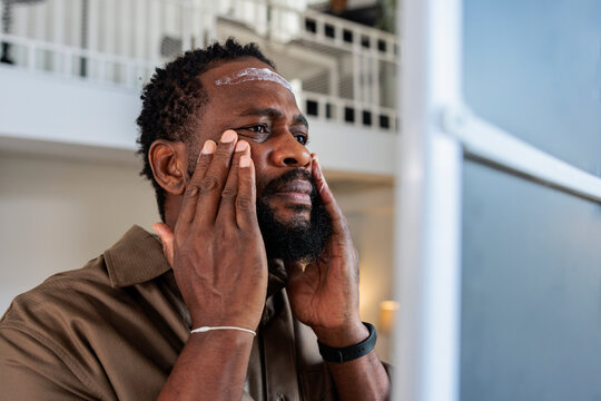 Man looking in mirror and applying moisturizer on face