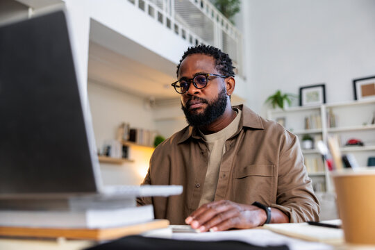 Serious man in eyeglasses using laptop while working from home