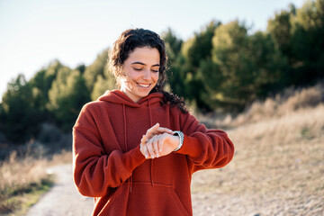 Smiling sportswoman checking smartwatch during training outside.
